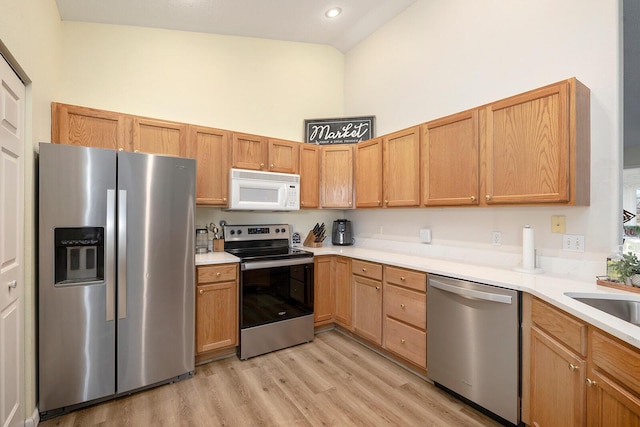 kitchen with high vaulted ceiling, appliances with stainless steel finishes, sink, and light hardwood / wood-style floors