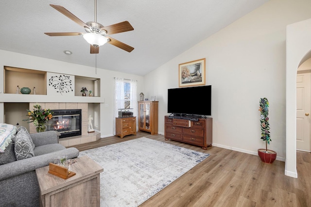 living room featuring a fireplace, lofted ceiling, light wood-type flooring, ceiling fan, and a textured ceiling