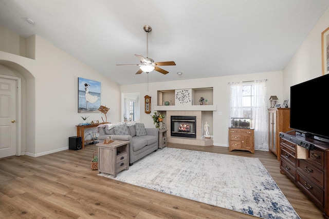 living room with a fireplace, lofted ceiling, light wood-type flooring, ceiling fan, and a textured ceiling