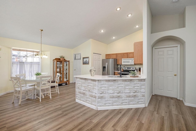 kitchen with appliances with stainless steel finishes, high vaulted ceiling, sink, hanging light fixtures, and light hardwood / wood-style flooring