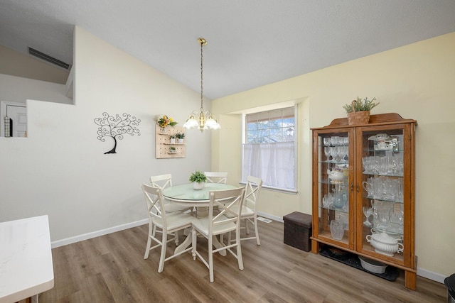 dining room with lofted ceiling, wood-type flooring, and a notable chandelier