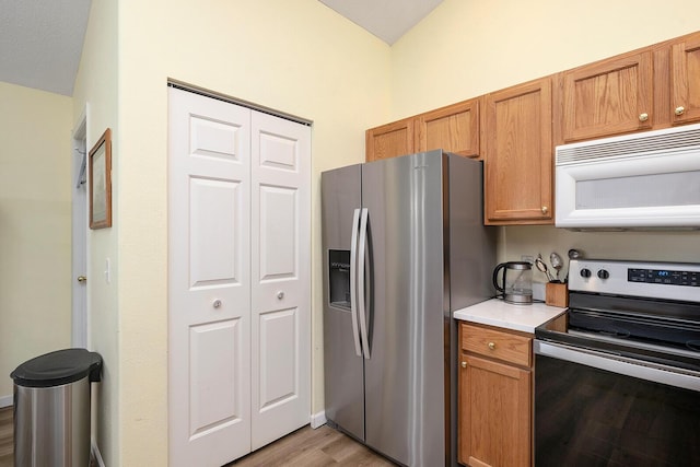 kitchen with stainless steel appliances, vaulted ceiling, and light wood-type flooring