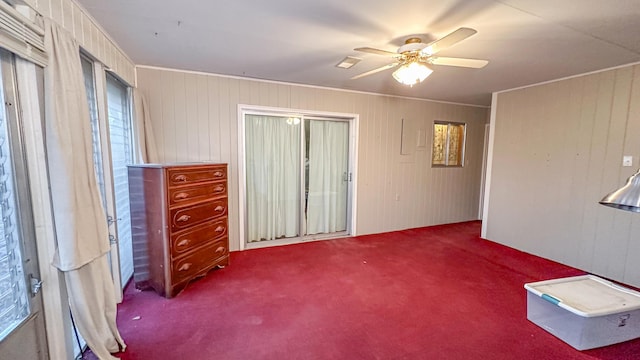 interior space with wood walls, ceiling fan, and carpet flooring