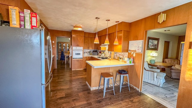 kitchen with pendant lighting, stainless steel fridge, a breakfast bar, white oven, and kitchen peninsula