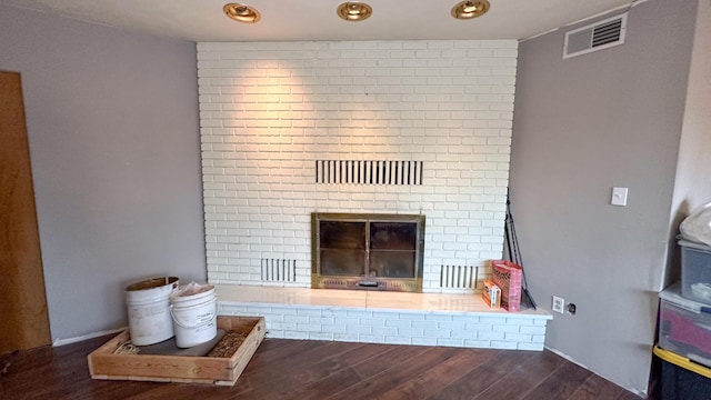 unfurnished living room featuring a brick fireplace and dark wood-type flooring