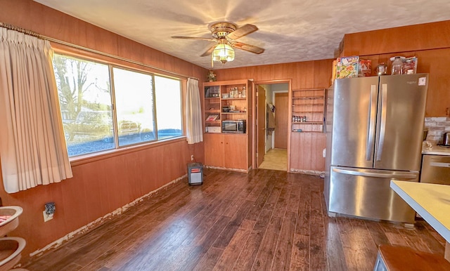 kitchen with dark hardwood / wood-style floors, wood walls, ceiling fan, stainless steel appliances, and a textured ceiling