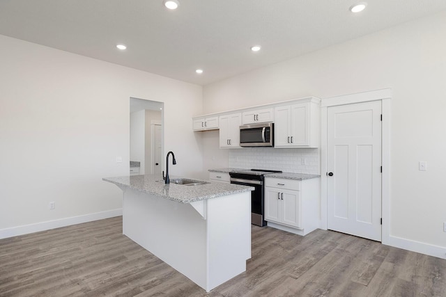 kitchen featuring sink, white cabinetry, light stone counters, electric stove, and a kitchen island with sink