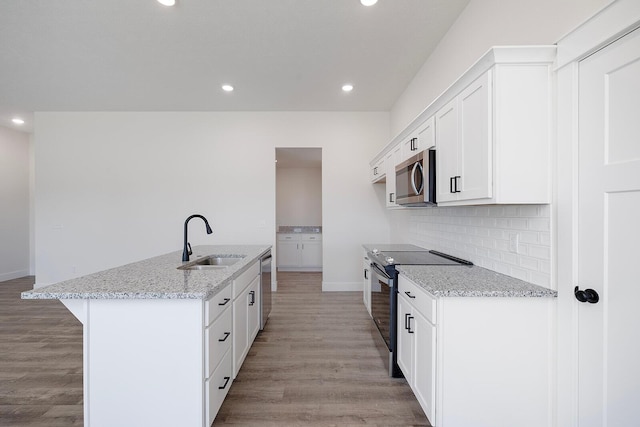 kitchen featuring appliances with stainless steel finishes, white cabinetry, sink, light stone counters, and a center island with sink