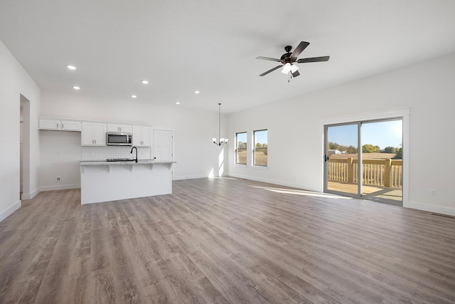 unfurnished living room featuring sink, ceiling fan with notable chandelier, and light hardwood / wood-style floors