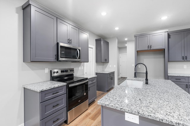 kitchen featuring sink, gray cabinets, stainless steel appliances, light stone counters, and light hardwood / wood-style floors