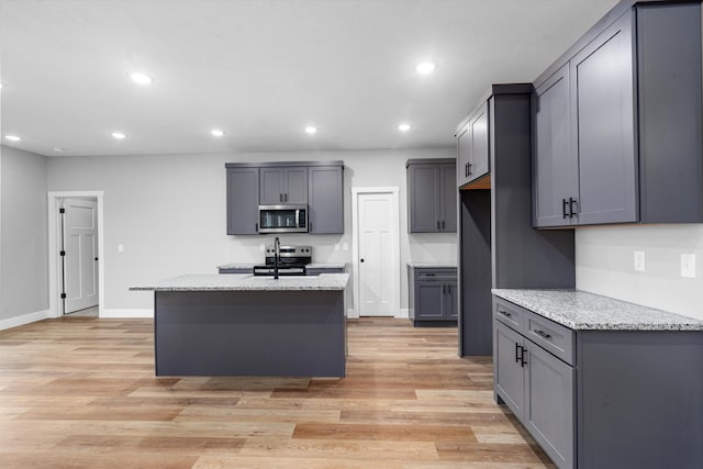 kitchen with a kitchen island with sink, gray cabinets, light stone countertops, and appliances with stainless steel finishes