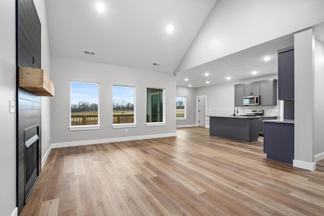 unfurnished living room featuring sink, light hardwood / wood-style floors, and high vaulted ceiling