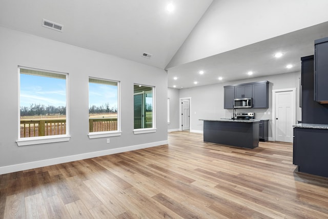 kitchen featuring a center island with sink, light stone counters, high vaulted ceiling, and light hardwood / wood-style floors