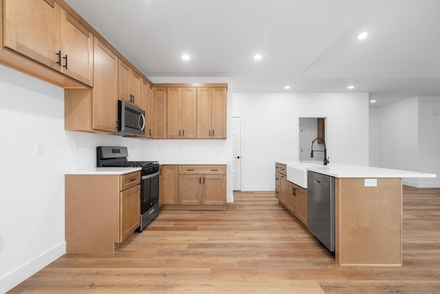 kitchen featuring an island with sink, stainless steel appliances, sink, and light hardwood / wood-style flooring