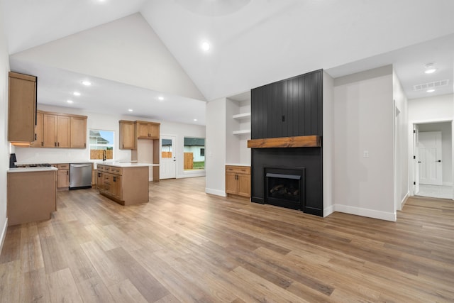 kitchen with stainless steel dishwasher, a kitchen island, a large fireplace, and light hardwood / wood-style flooring