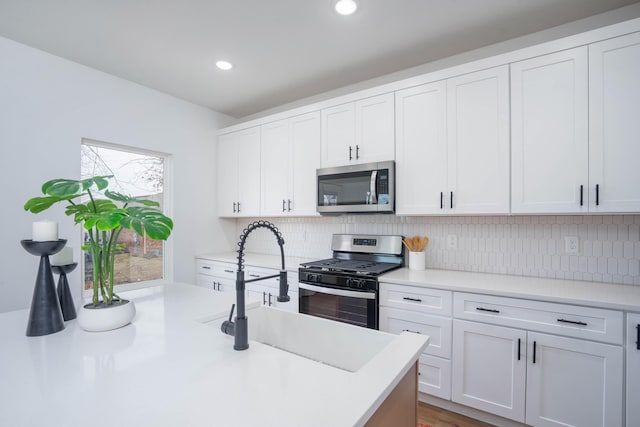 kitchen with light countertops, a sink, white cabinetry, tasteful backsplash, and appliances with stainless steel finishes