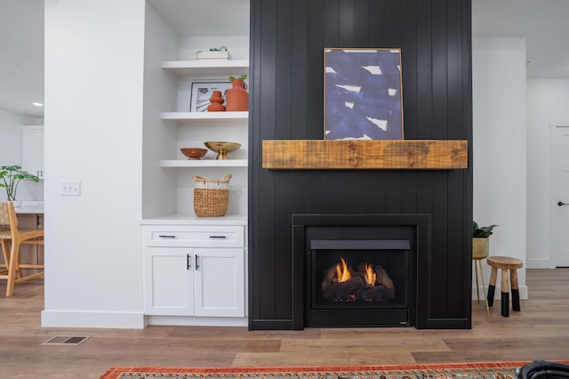 interior details featuring wood finished floors, a large fireplace, built in features, baseboards, and visible vents