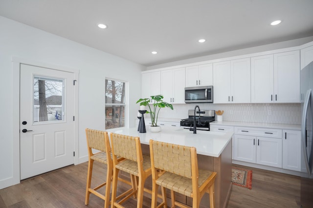 kitchen featuring a kitchen breakfast bar, white cabinetry, tasteful backsplash, stainless steel appliances, and dark wood-type flooring