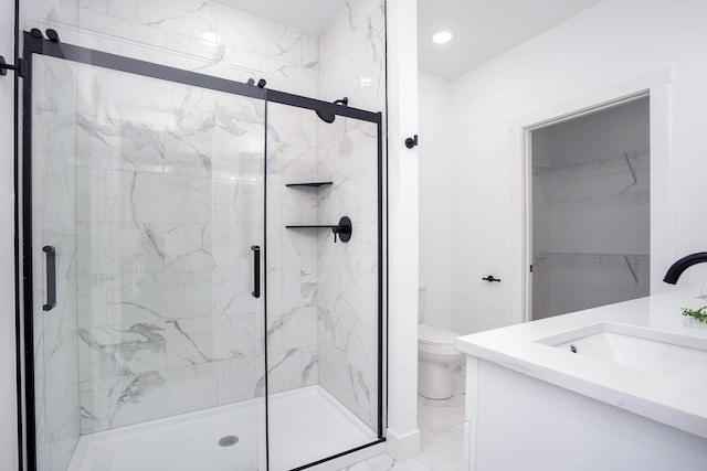 bathroom featuring marble finish floor, a marble finish shower, toilet, vanity, and a walk in closet
