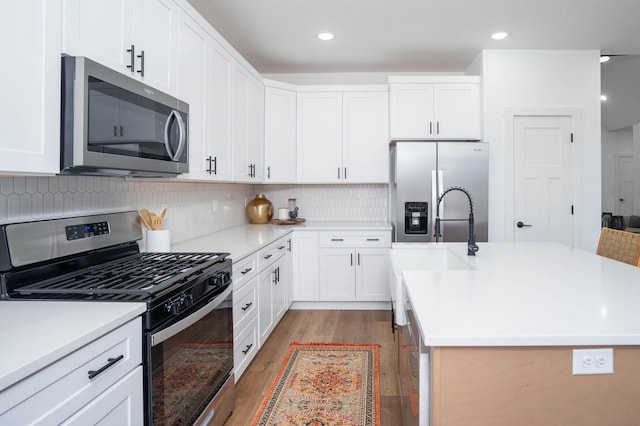 kitchen with light countertops, a kitchen island with sink, wood finished floors, stainless steel appliances, and tasteful backsplash