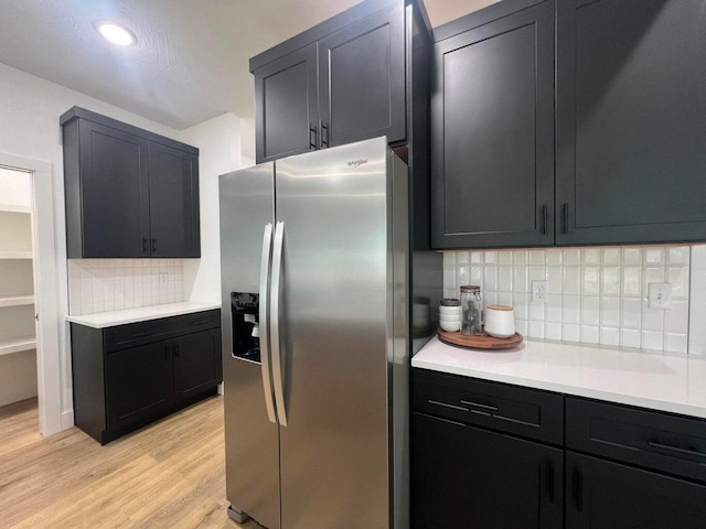 kitchen featuring stainless steel refrigerator with ice dispenser, light wood-type flooring, and decorative backsplash