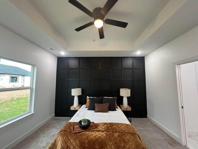 bedroom with light colored carpet, ceiling fan, and a tray ceiling