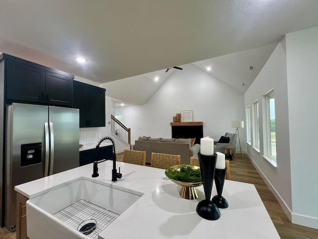 kitchen with sink, stainless steel fridge, hardwood / wood-style floors, decorative backsplash, and vaulted ceiling