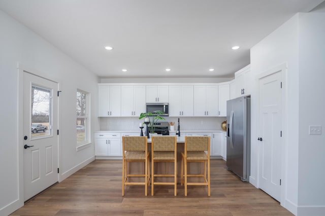 kitchen with tasteful backsplash, white cabinets, a kitchen breakfast bar, stainless steel appliances, and a center island with sink