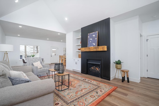 living room featuring a fireplace, high vaulted ceiling, built in features, and light wood-type flooring