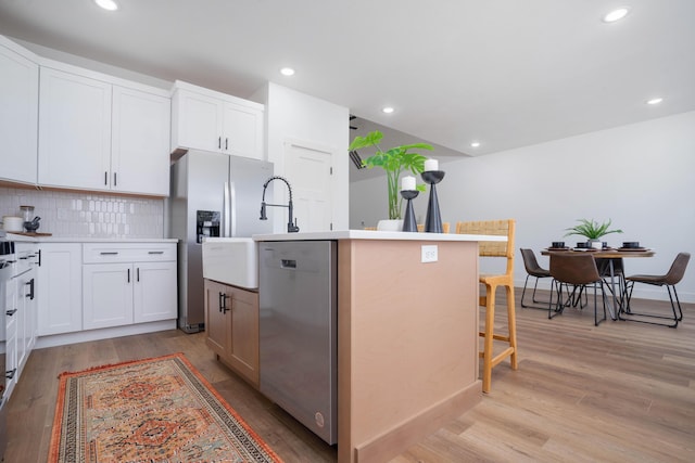 kitchen with a breakfast bar, white cabinetry, appliances with stainless steel finishes, a kitchen island with sink, and decorative backsplash