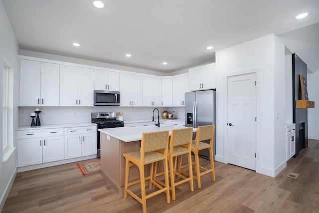 kitchen with backsplash, white cabinets, a kitchen bar, a kitchen island with sink, and stainless steel appliances