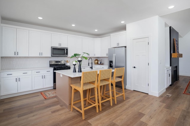 kitchen with appliances with stainless steel finishes, white cabinetry, light hardwood / wood-style floors, an island with sink, and a kitchen bar