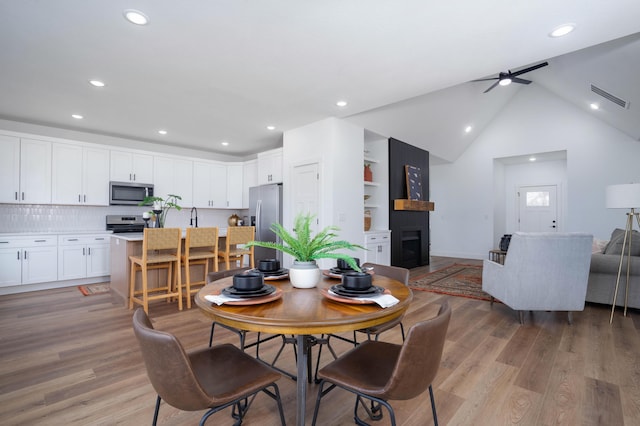 dining room featuring vaulted ceiling, a large fireplace, ceiling fan, and light wood-type flooring