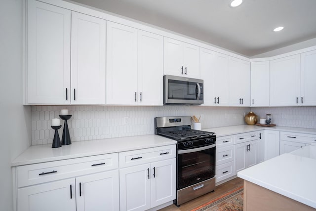 kitchen with tasteful backsplash, dark hardwood / wood-style flooring, white cabinets, and appliances with stainless steel finishes