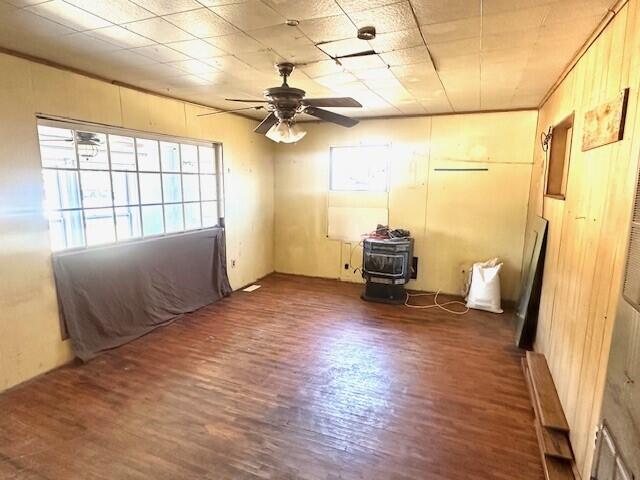 spare room featuring dark wood-type flooring, ceiling fan, and a wood stove