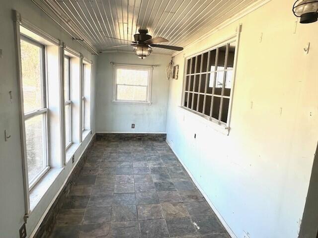 unfurnished sunroom featuring ceiling fan, plenty of natural light, and wooden ceiling