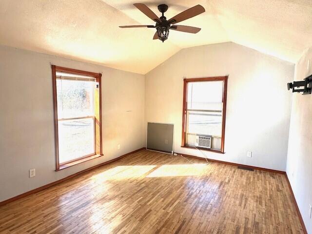 additional living space with cooling unit, hardwood / wood-style floors, vaulted ceiling, and ceiling fan