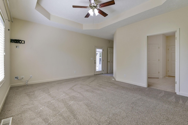 carpeted empty room with a healthy amount of sunlight, ceiling fan, and a tray ceiling