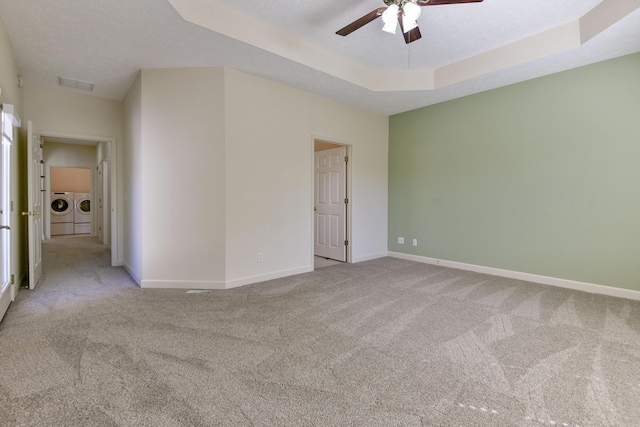 empty room with ceiling fan, a textured ceiling, separate washer and dryer, light colored carpet, and a raised ceiling