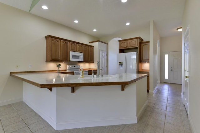 kitchen with light tile patterned floors, white appliances, kitchen peninsula, and a kitchen bar