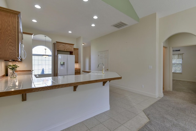 kitchen featuring a breakfast bar area, light tile patterned floors, tile counters, kitchen peninsula, and white appliances