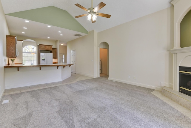 unfurnished living room with a tile fireplace, high vaulted ceiling, light carpet, and ceiling fan