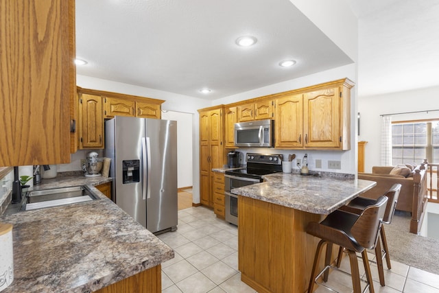 kitchen featuring sink, light tile patterned floors, a breakfast bar area, stainless steel appliances, and dark stone counters