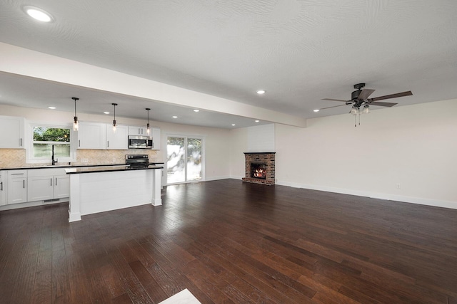 unfurnished living room with sink, dark wood-type flooring, a brick fireplace, and ceiling fan