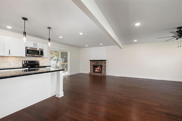 kitchen with appliances with stainless steel finishes, a fireplace, decorative light fixtures, tasteful backsplash, and white cabinetry