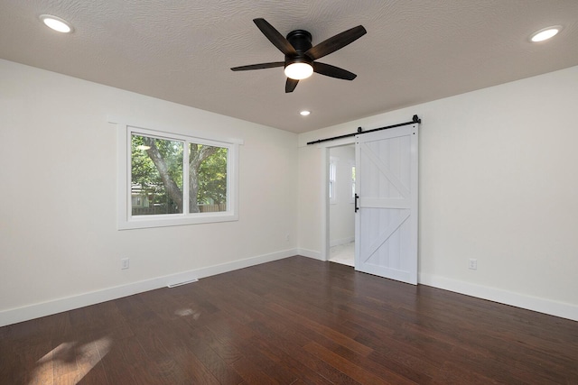 empty room with ceiling fan, a barn door, dark hardwood / wood-style flooring, and a textured ceiling