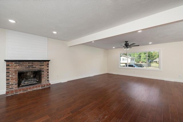 unfurnished living room featuring dark hardwood / wood-style flooring, a brick fireplace, ceiling fan, and a textured ceiling