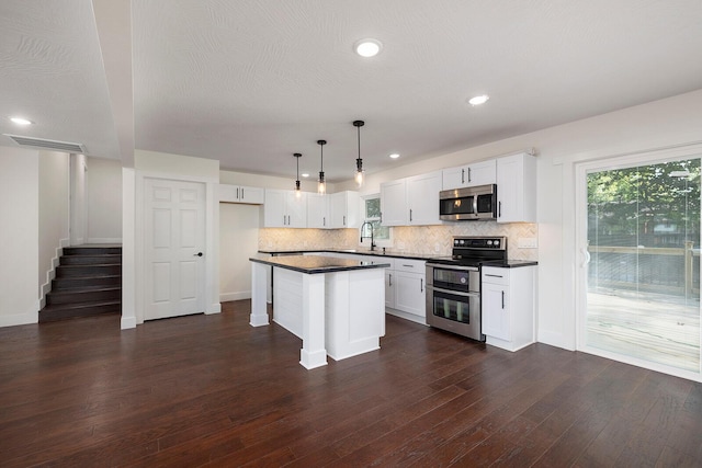 kitchen with pendant lighting, appliances with stainless steel finishes, a center island, white cabinets, and dark hardwood / wood-style flooring