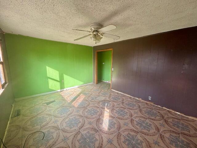 unfurnished room featuring ceiling fan, a textured ceiling, and wood walls