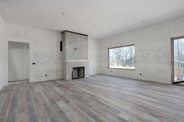 unfurnished living room featuring a healthy amount of sunlight, a large fireplace, and light wood-type flooring